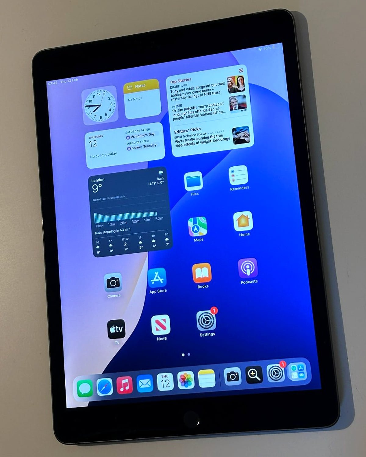 An iPad with the home screen on, lying on a desk