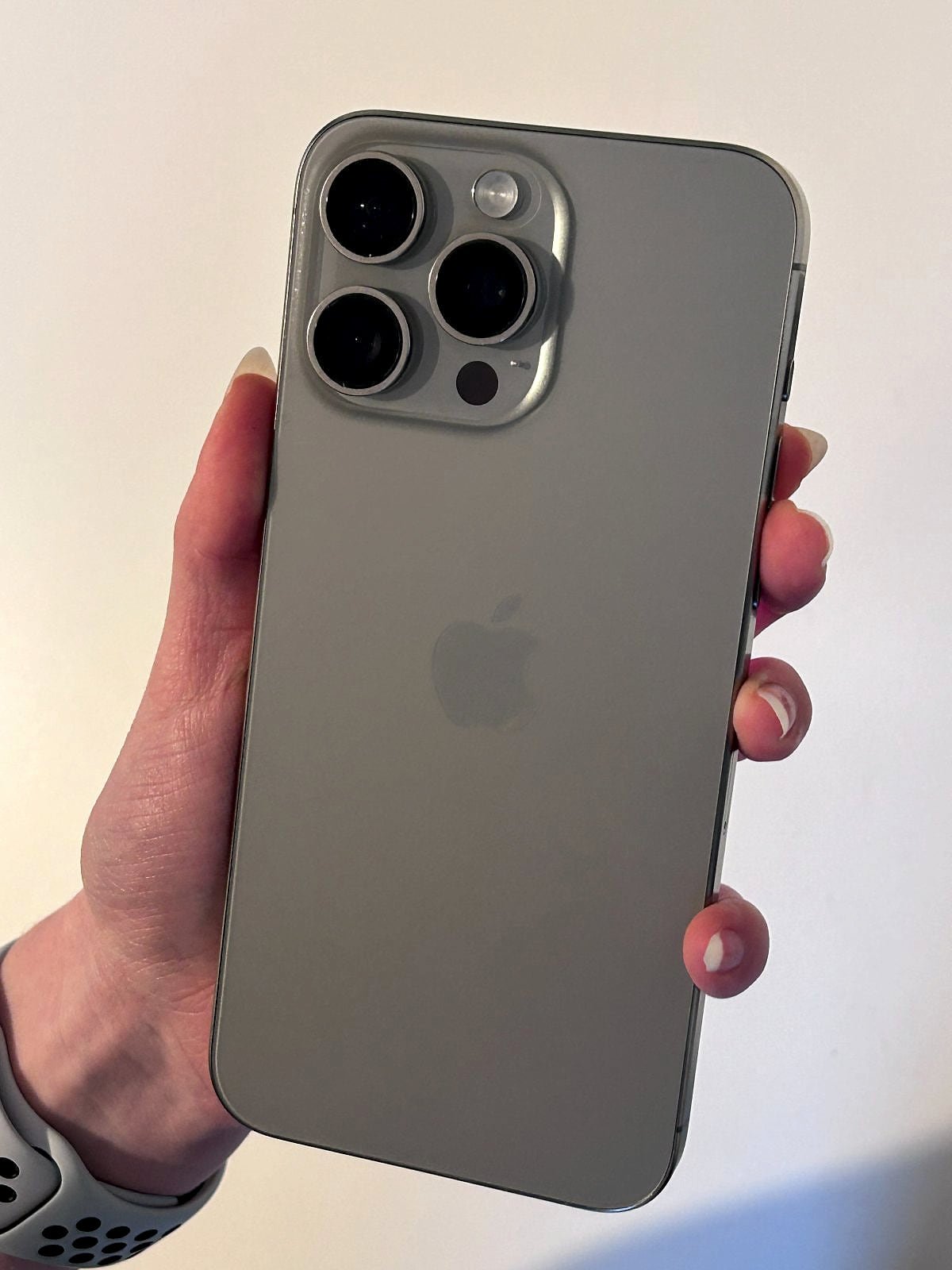 iPhone 15 Pro in natural titanium, held up to show the back