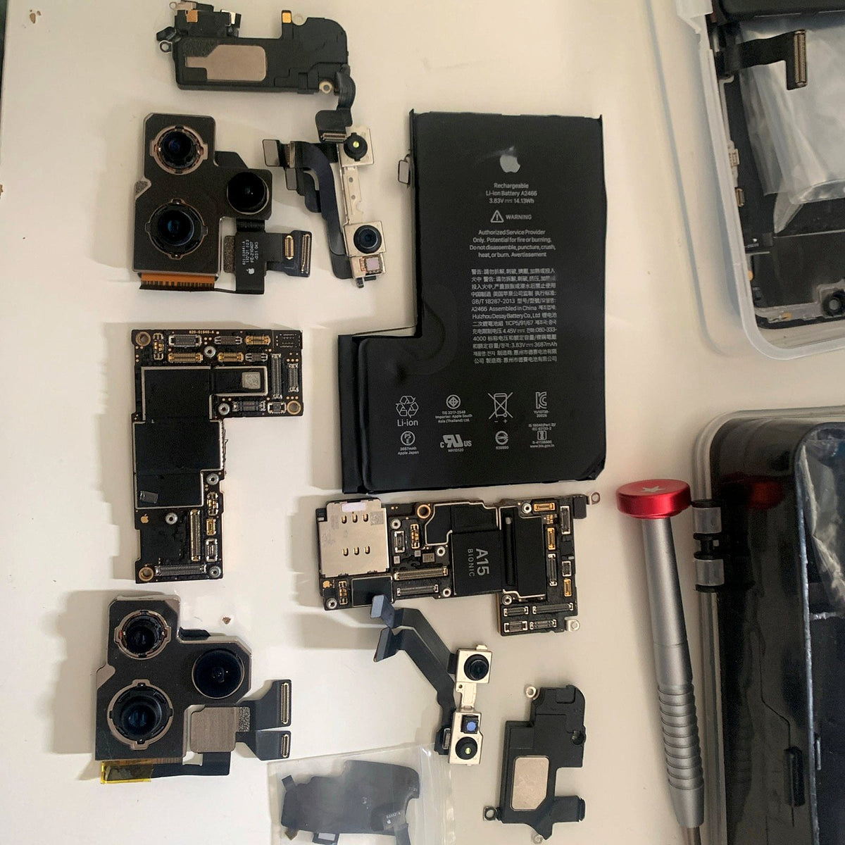 Phone parts laid out on the bench: cameras, battery, logic board, tools