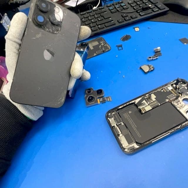 A gloved hand holding an iPhone over an open one on the bench, mid-repair