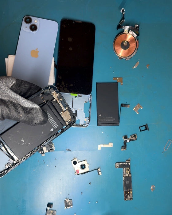 A gloved hand lifting an opened iPhone over the parts of a stripped iPhone 14 on the bench.